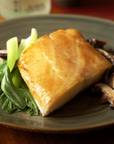 Plated black cod with greens and mushrooms on a wooden table.