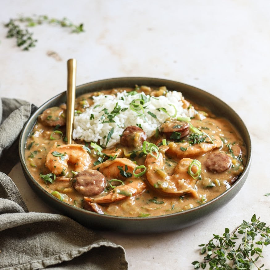 Shrimp gumbo with rice and a gold spoon in a shallow bowl on a white background with herbs and a towel