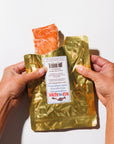 Gold packaging of smoked salmon with a label held by hands on a white background