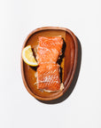 Smoked salmon portion on a wooden plate with a cut lemon on a white background
