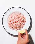 Salad shrimp in a shallow white bowl with a hand squeezing lemon on a white background