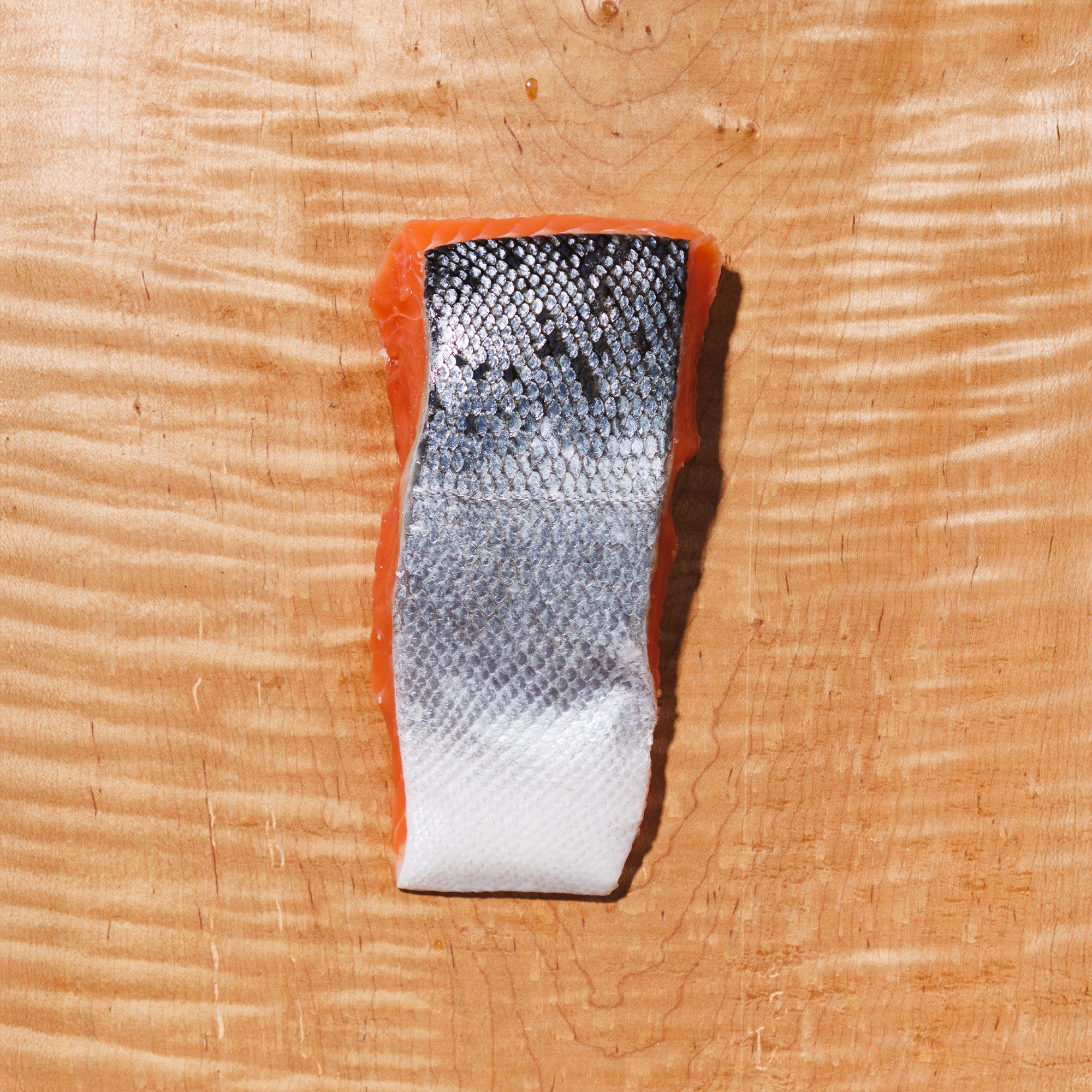 raw coho salmon portion skin side up on a wooden cutting board