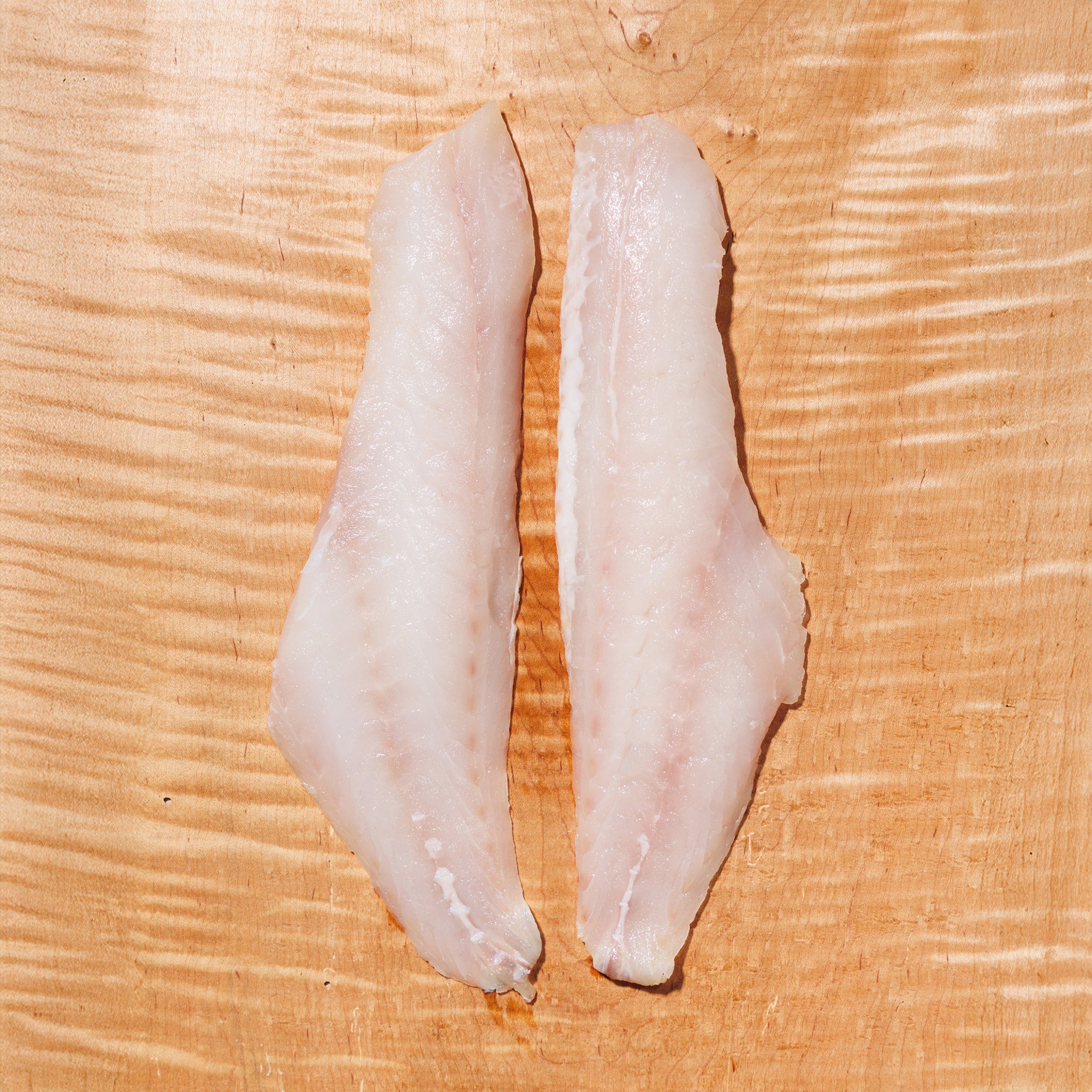 Two raw rockfish fillets on a wooden cutting board