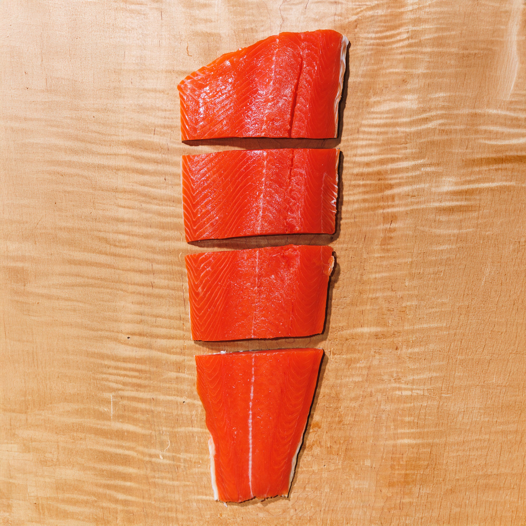 Four portions of raw sockeye salmon on a wooden cutting board, making up a full fillet