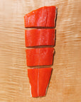 Four portions of raw sockeye salmon on a wooden cutting board, making up a full fillet