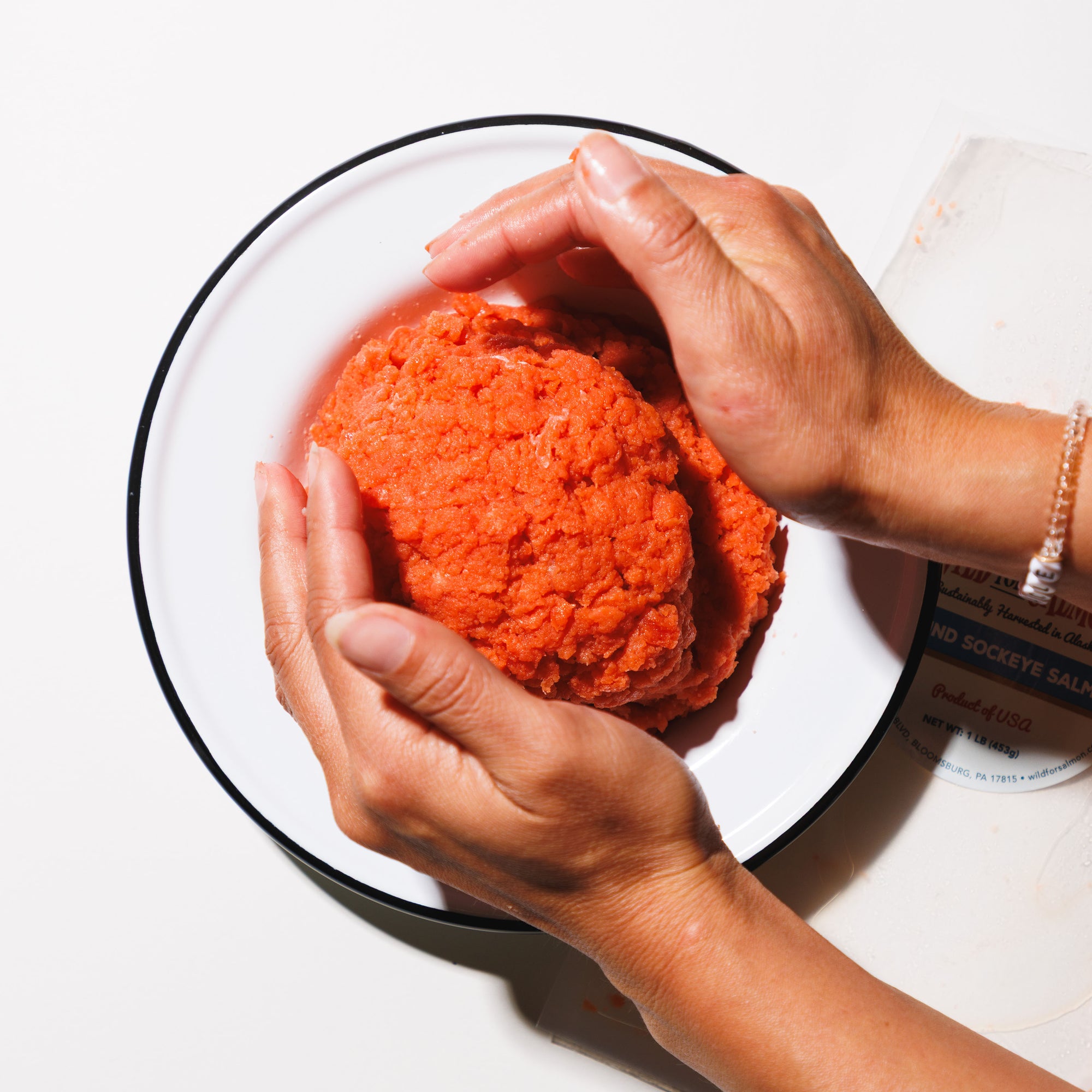 Person shaping wild ground sockeye into a large ball on a white plate with a white background