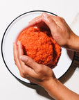 Person shaping wild ground sockeye into a large ball on a white plate with a white background