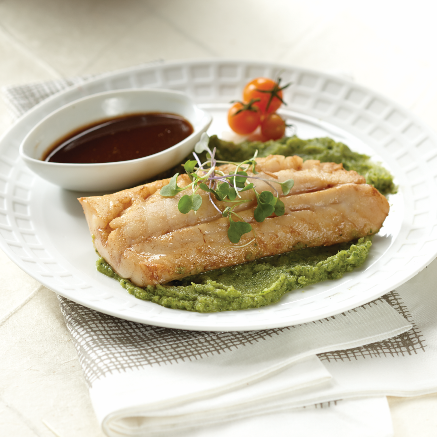 Plated dish of rockfish with green sauce and a side of cherry tomatoes on a white plate.