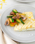 Plated dish of grilled halibut with zucchini, mushrooms, and tomatoes on a light background