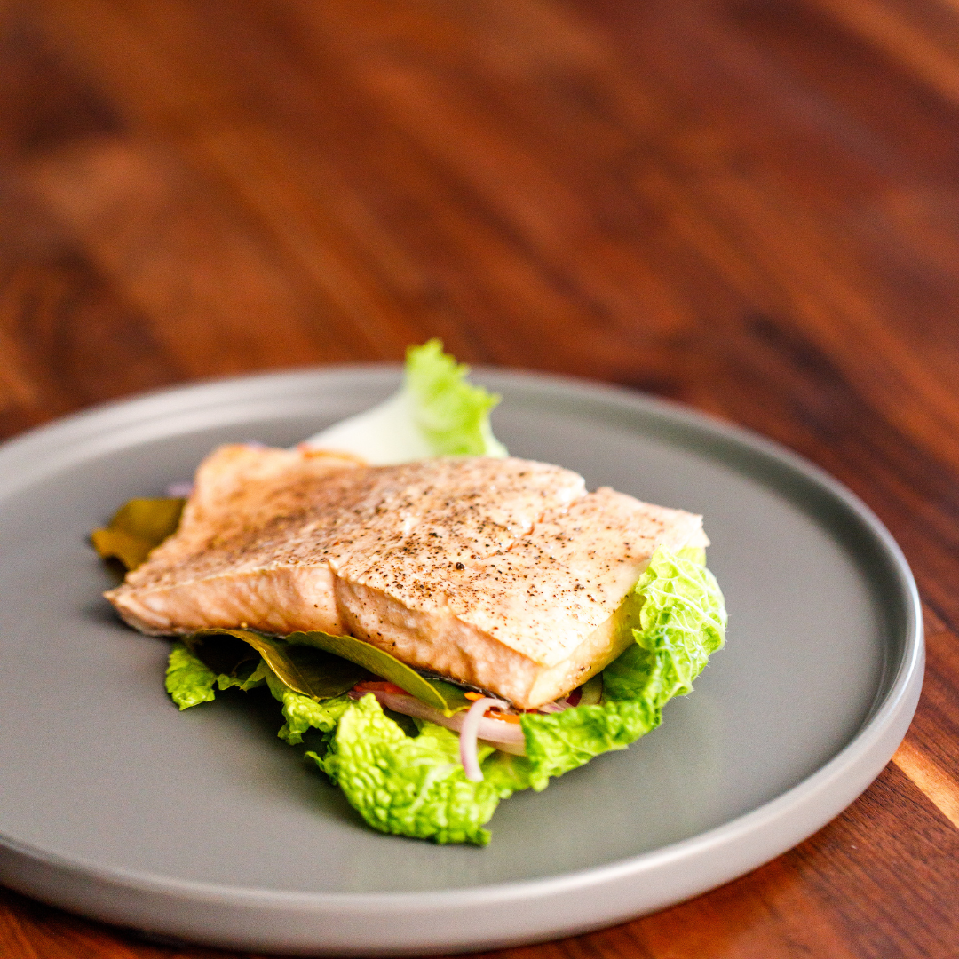 Keta Salmon portion on a bed of lettuce on a gray plate with a wooden background