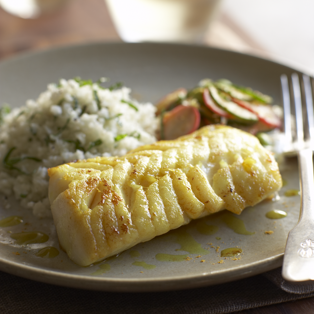 Plated dish with Pacific cod, rice, and salad on a wooden table.