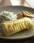 Plated dish with Pacific cod, rice, and salad on a wooden table.