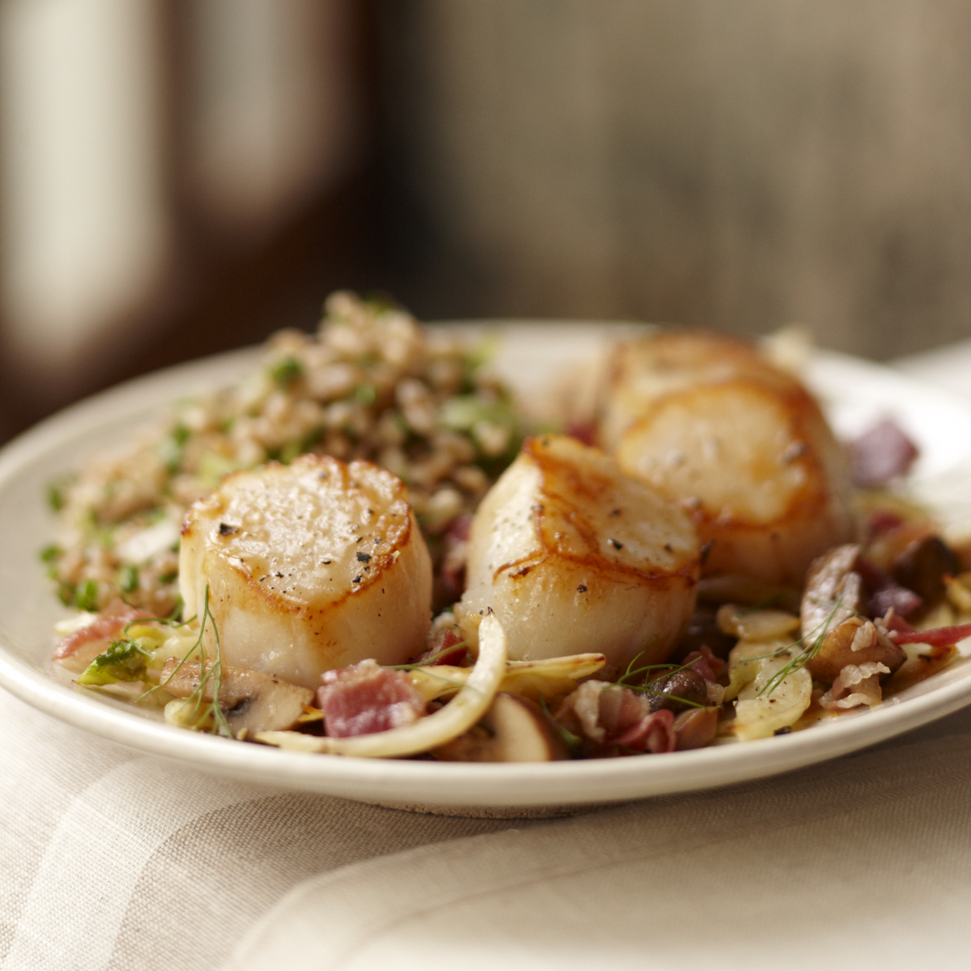 Plated dish of scallops with a side of rice and vegetables on a neutral background