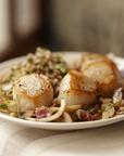 Plated dish of scallops with a side of rice and vegetables on a neutral background
