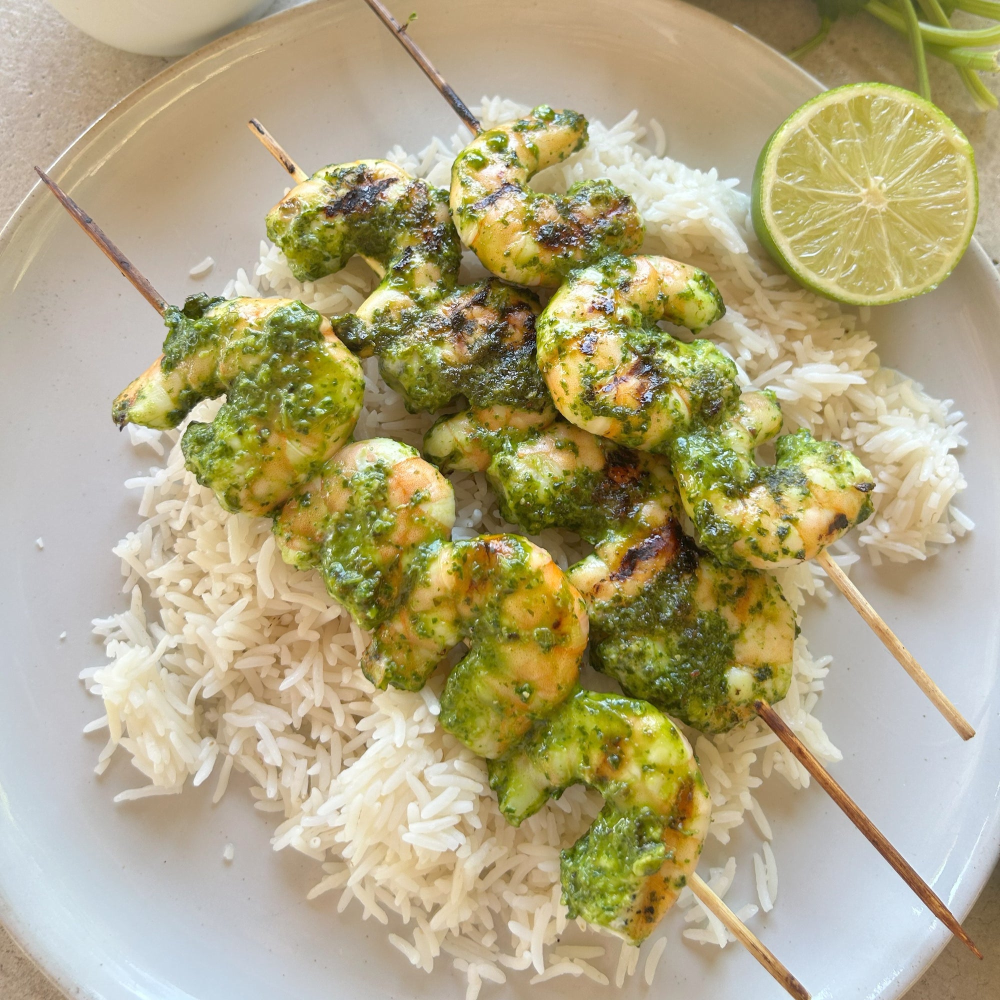 Shrimp Skewers with chimichurri sauce over rice on a white plate with a lime and a light background