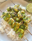 Shrimp Skewers with chimichurri sauce over rice on a white plate with a lime and a light background