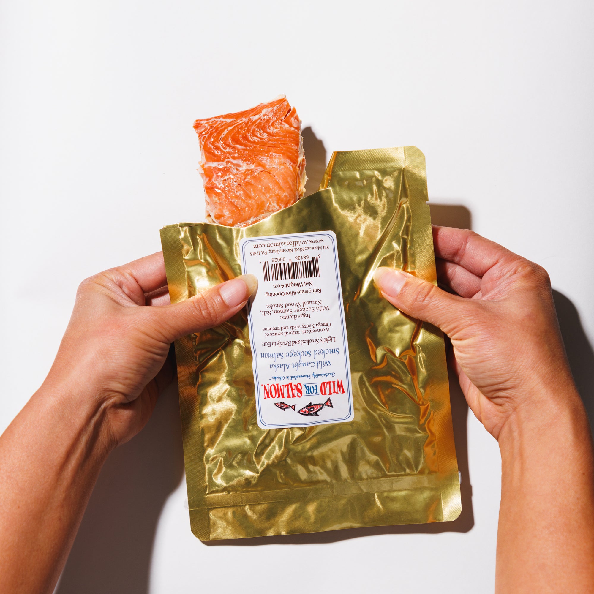 Gold packaging of smoked salmon with a label held by hands on a white background