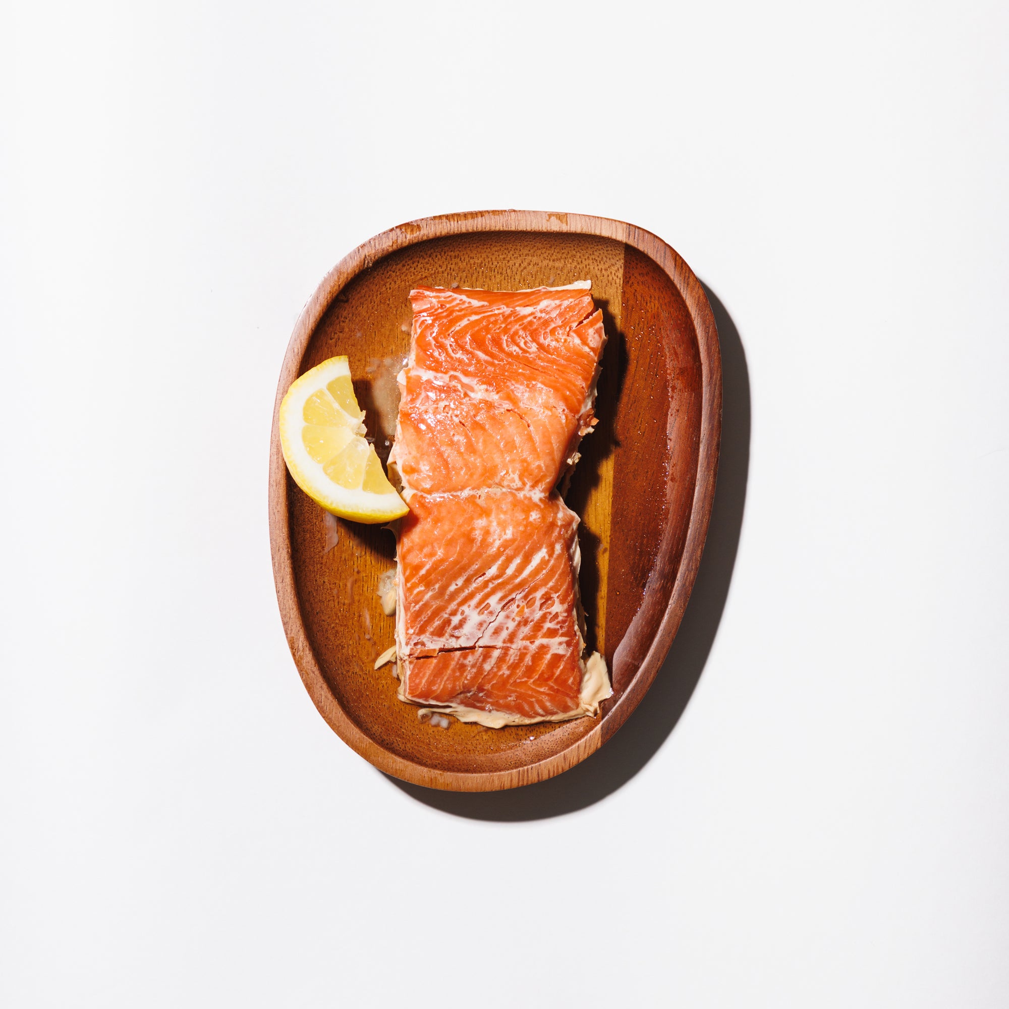 Smoked salmon portion on a wooden plate  with a cut lemon on a white background