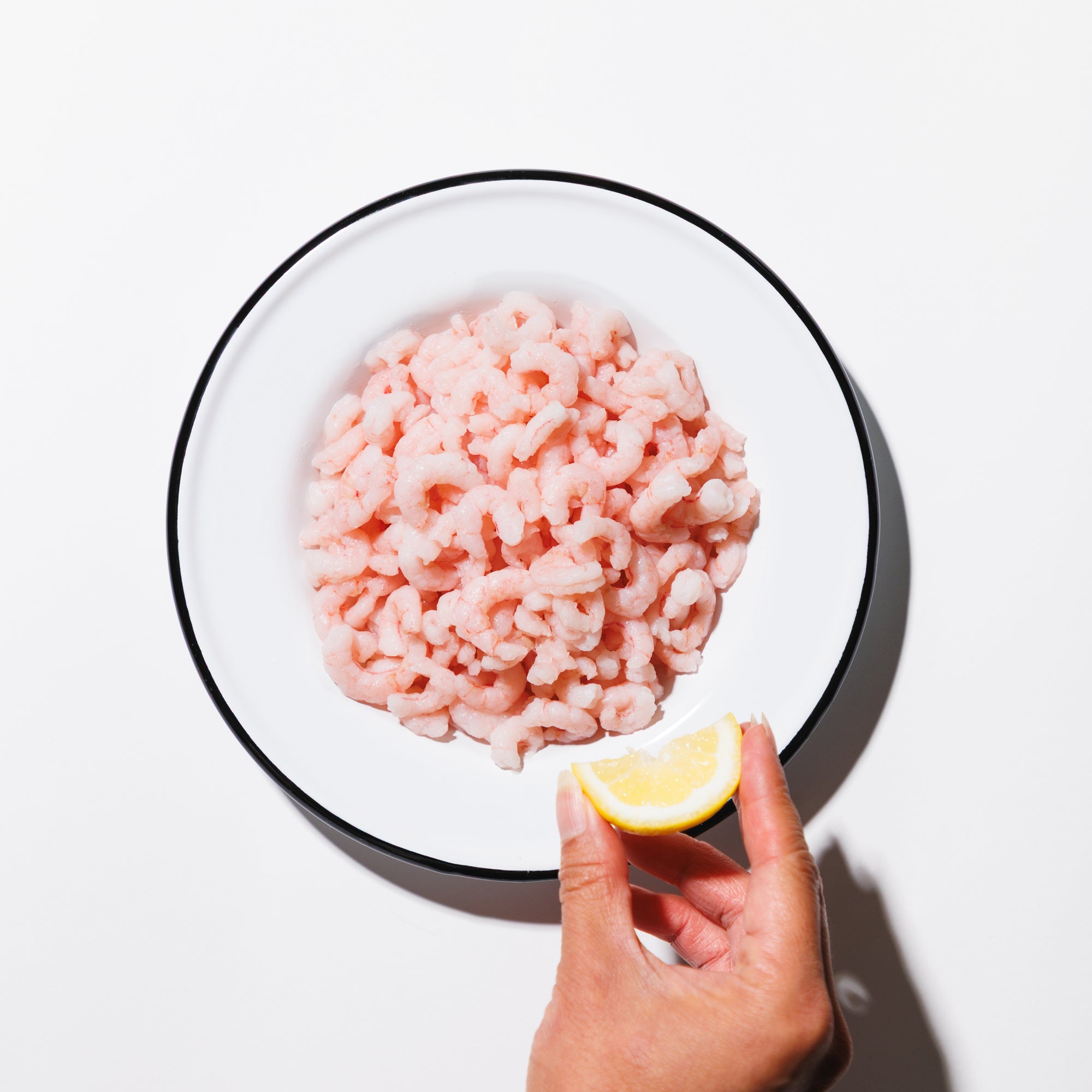 Salad shrimp in a shallow white bowl with a hand squeezing lemon on a white background