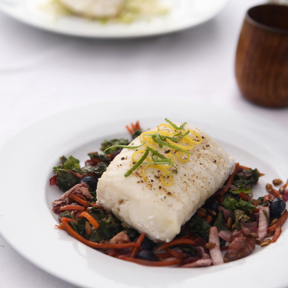 Plated dish of wild ling cod over a bed of vegetables on a white plate.