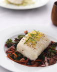 Plated dish of wild ling cod over a bed of vegetables on a white plate.