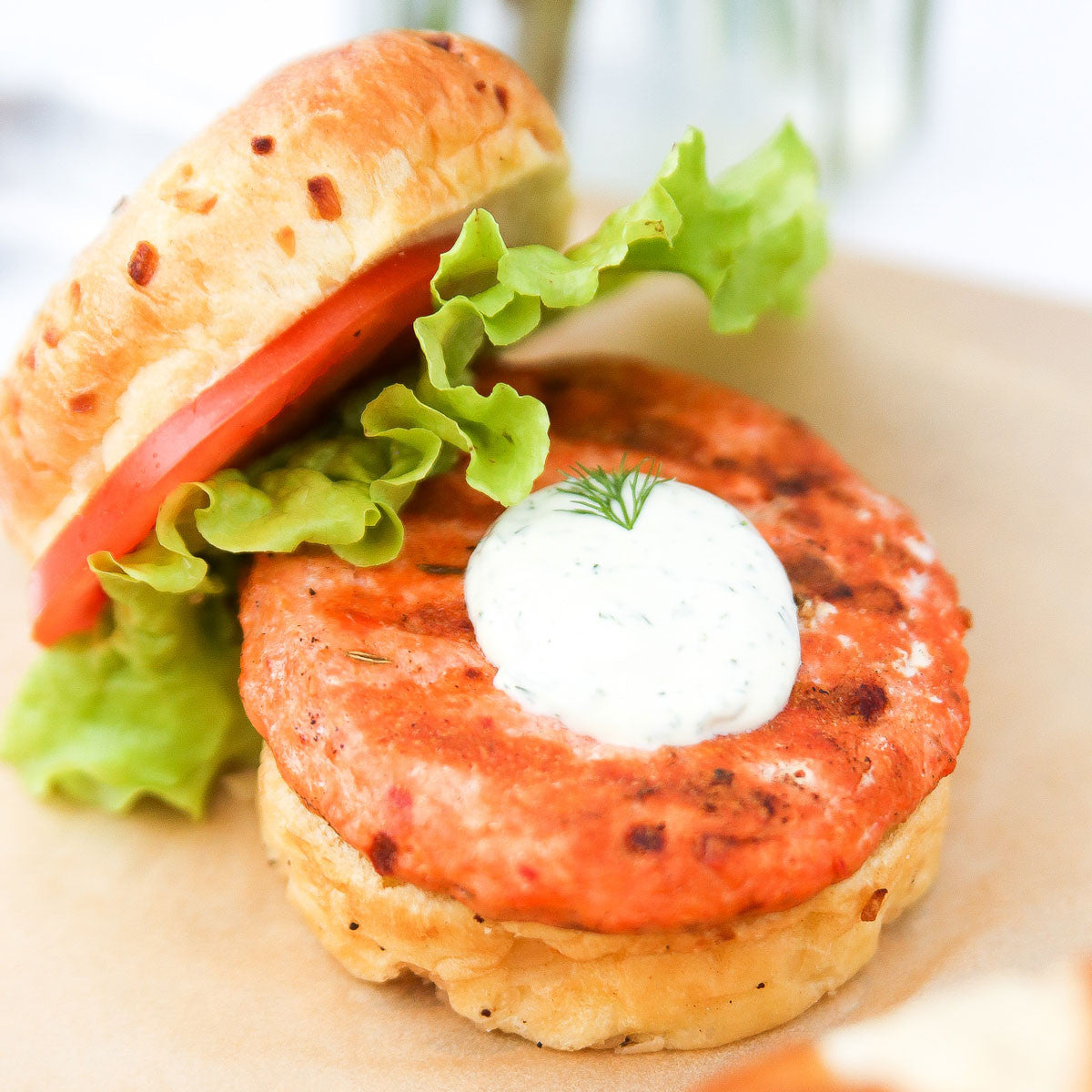 Close-up of a salmon burger with lettuce and tomato on a bun.