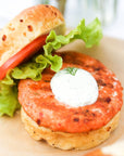 Close-up of a salmon burger with lettuce and tomato on a bun.